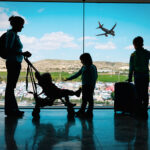 mother with kids and luggage looking at planes in airport, family travel